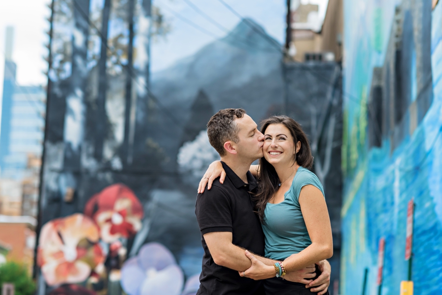 A man kisses his girlfriend in front of a beautiful mural in Philly.